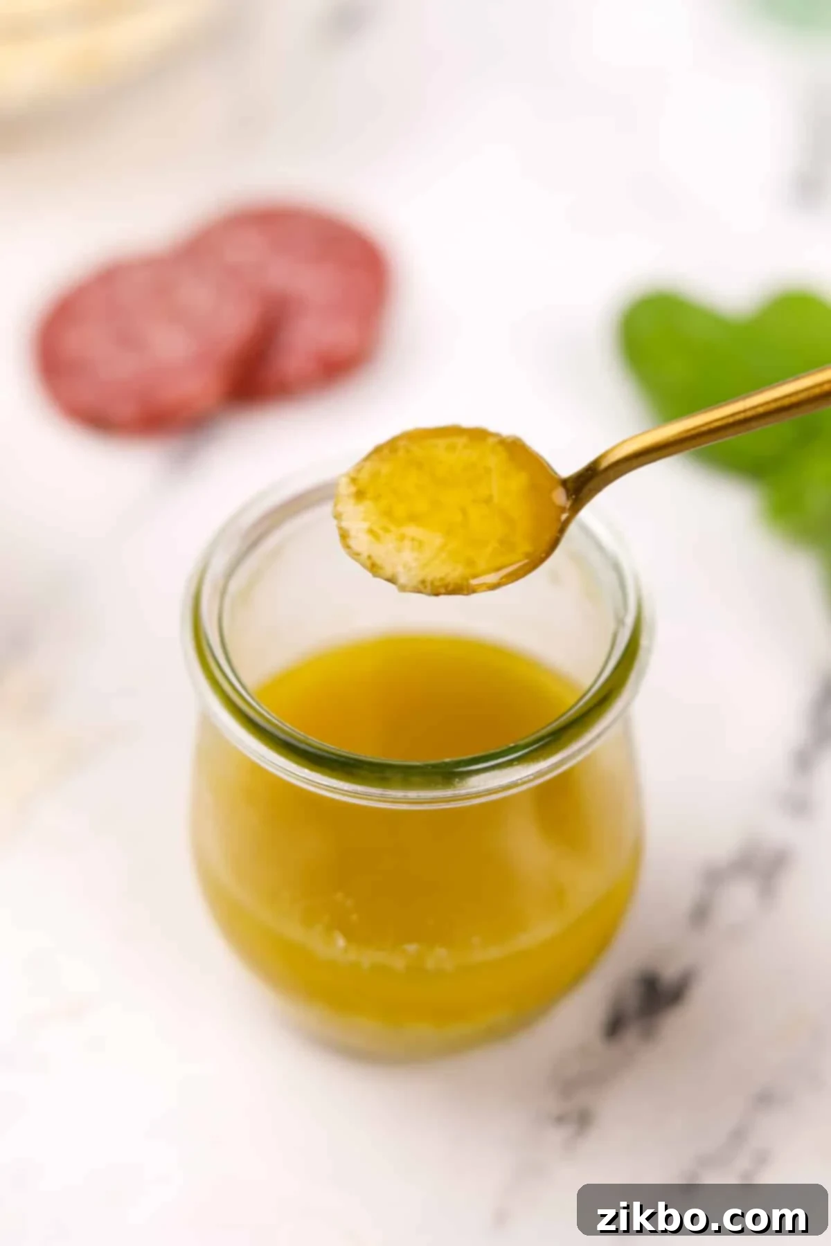 Leon's Artisan Blend 8 A small spoon holding a tiny amount of bright, golden vinaigrette, taken from a glass jar of Leon dressing, emphasizing its smooth texture.