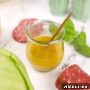Leon's Artisan Blend 10 A small glass jar of homemade vinaigrette with a small spoon inside, ready to be served over a fresh salad.