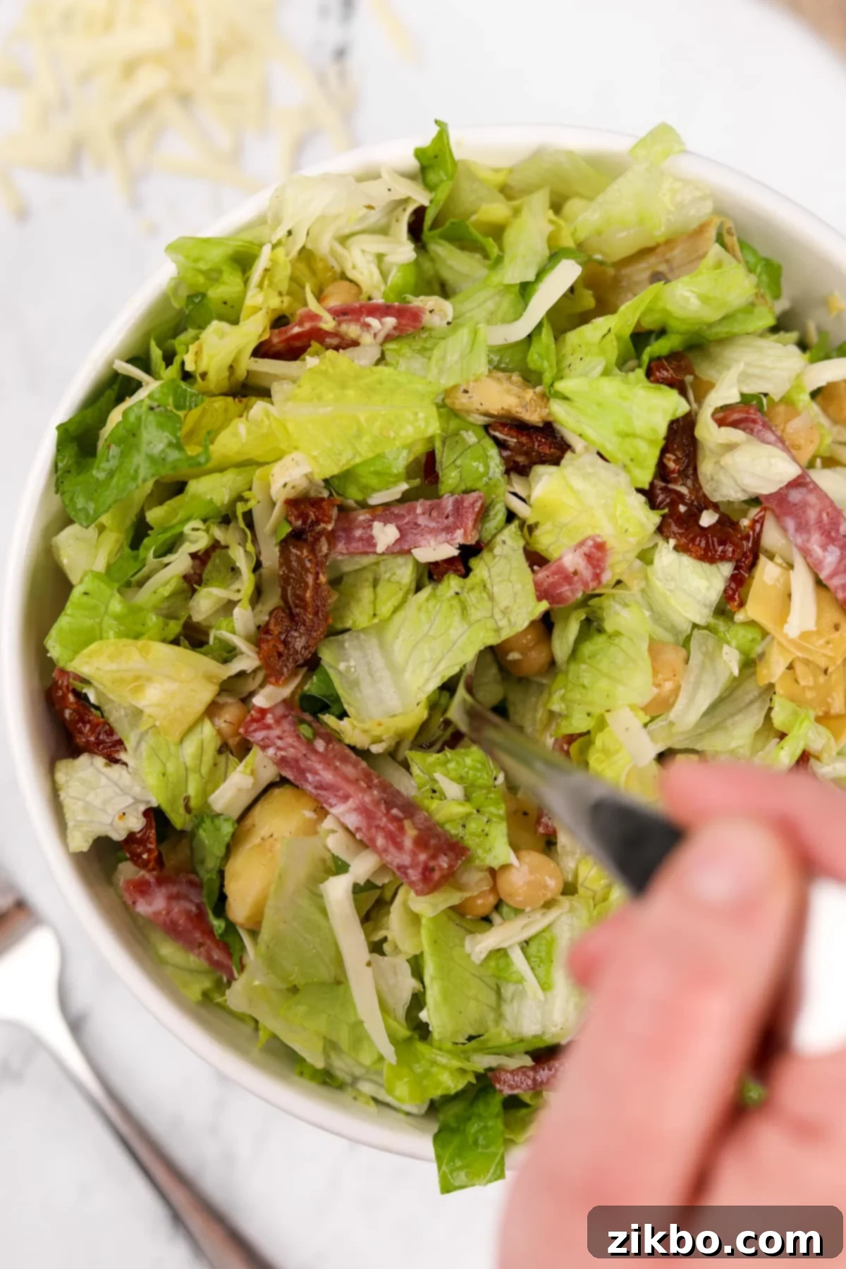 A close-up shot of a fork digging into a vibrant bowl of La Scala Chopped Salad, highlighting the mix of greens, salami, and mozzarella, ready to be enjoyed.