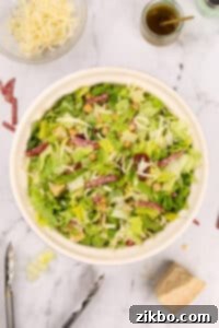 A bowl of chopped salad featuring chopped salami pieces evenly mixed with greens.
