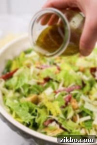 Pouring the homemade Leon salad dressing over the colorful chopped salad.