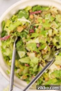 Tossing a vibrant chopped salad with tongs to evenly distribute the dressing.