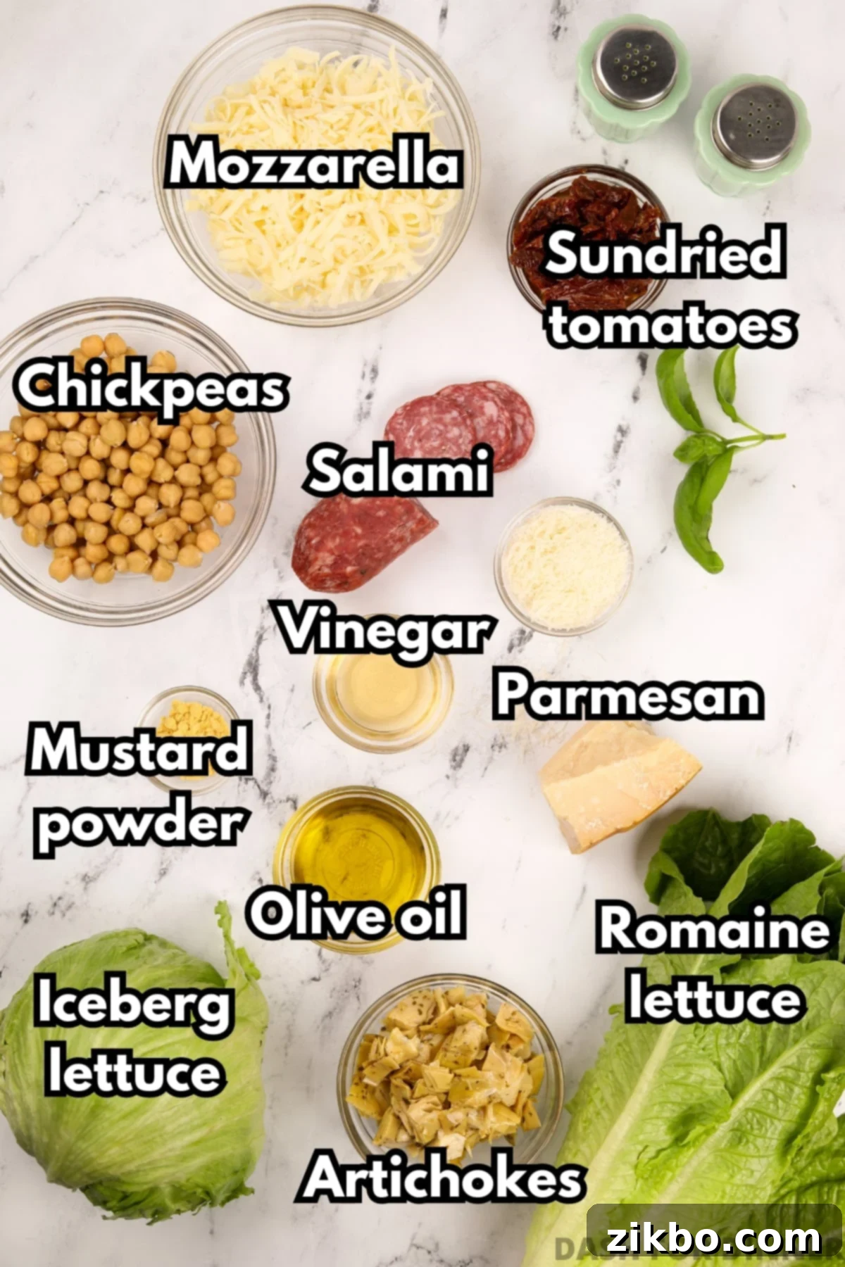 A flat lay photograph showcasing all the fresh and delicious ingredients required to make the ultimate chopped salad, including sliced salami, vibrant chickpeas, creamy mozzarella, juicy sun-dried tomatoes, grated parmesan cheese, and crisp lettuce.