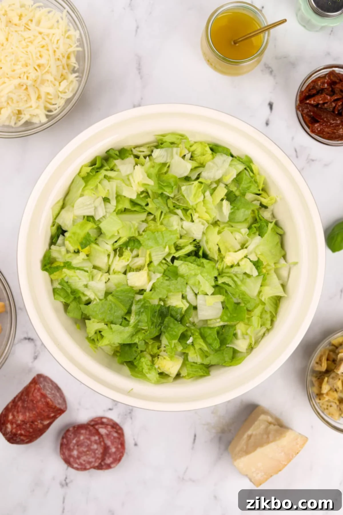 A large, clear glass bowl filled with finely chopped romaine and iceberg lettuce, ready for the other salad ingredients.