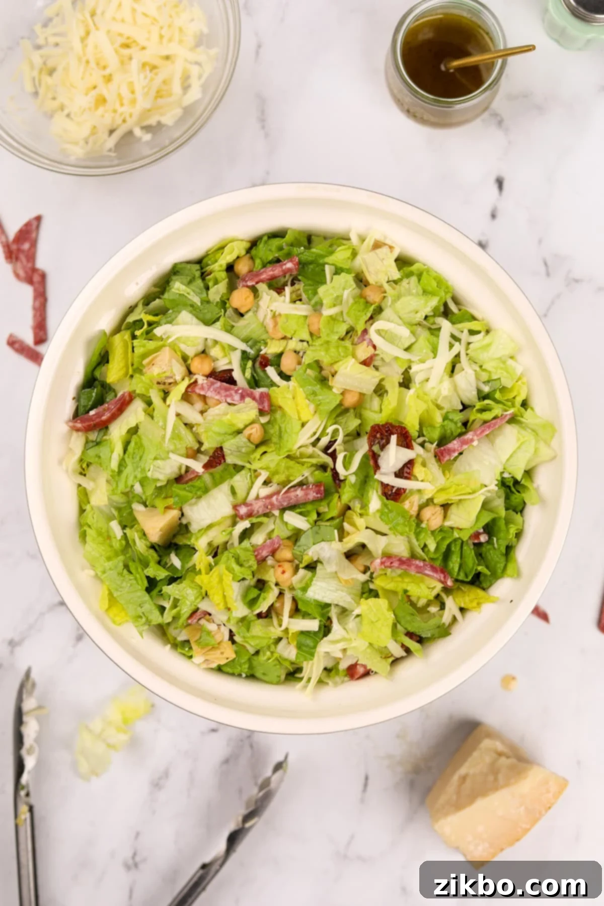 A close-up shot of a bowl of freshly prepared chopped salad, highlighting the perfectly diced salami pieces mixed among the crisp greens and other ingredients.