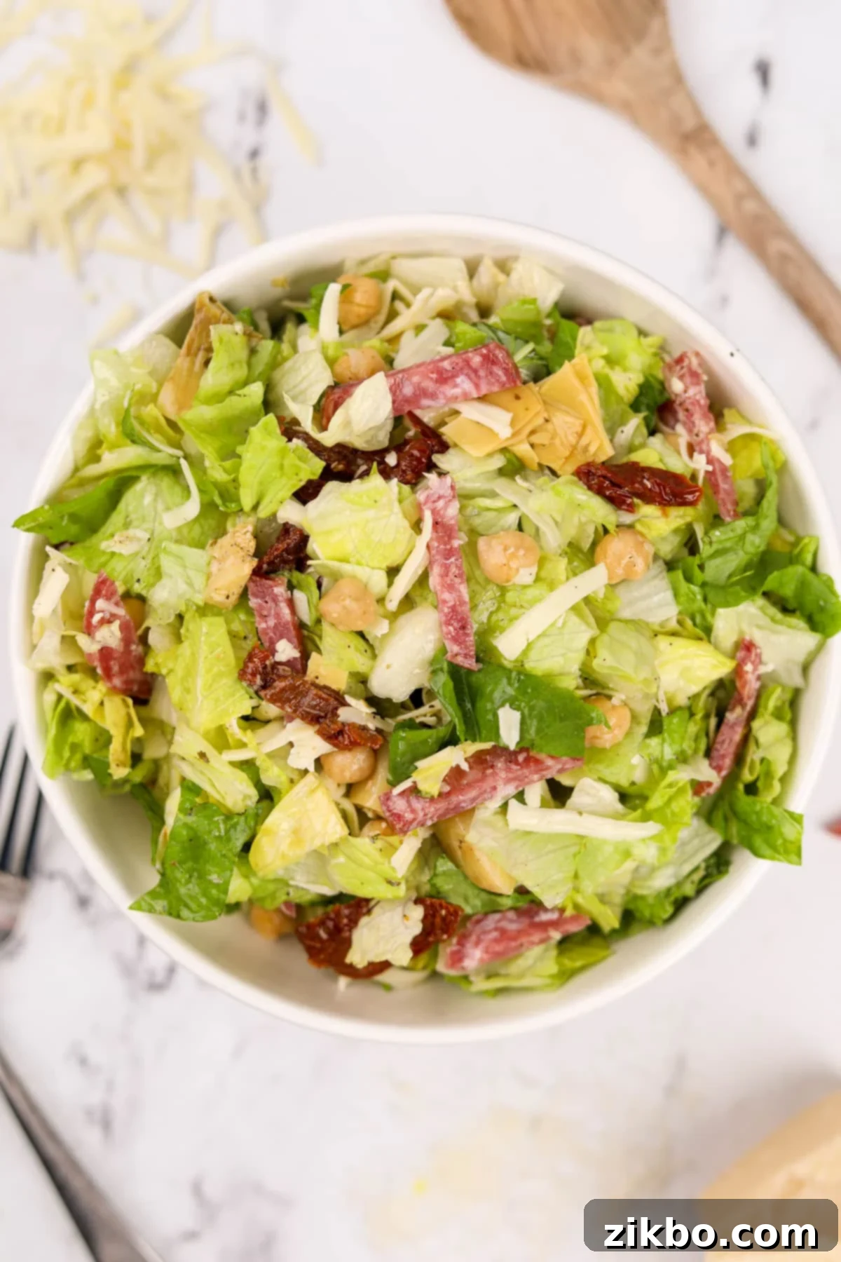 A large, inviting bowl of chopped Italian Salad, showcasing generous slices of salami and creamy mozzarella beautifully mixed with fresh greens and other vibrant toppings.