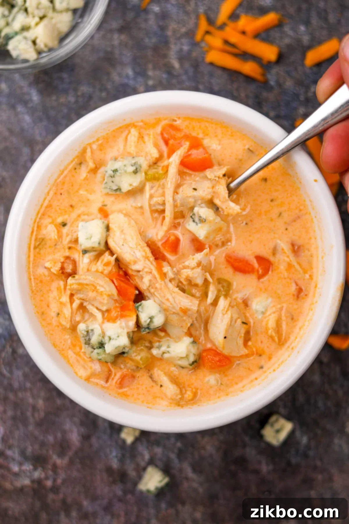 Bold Buffalo Chicken Soup 8 A bowl of spicy chicken soup with a spoon taking a portion, showcasing its creamy texture and rich color.