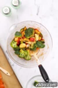 A large bowl with seasoned vegetables being stirred.