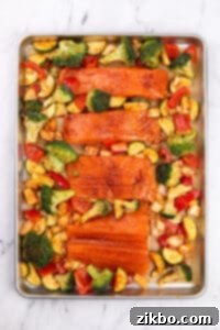 A sheet pan with seasoned salmon fillets and various vegetables.