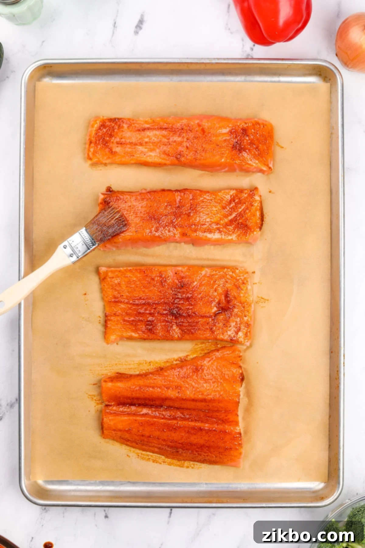 Effortless Sheet Pan Salmon Feast 5 Salmon fillets being brushed with the golden, seasoned oil mixture on a parchment-lined sheet pan.