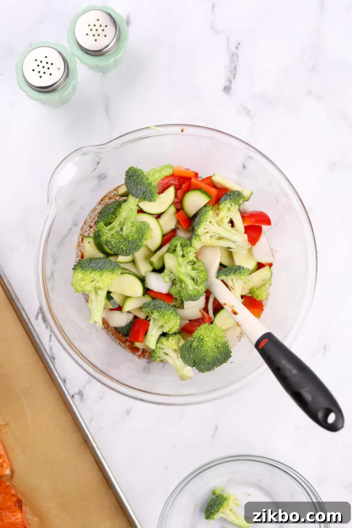 Effortless Sheet Pan Salmon Feast 6 A large bowl containing prepped vegetables: broccoli florets, sliced red bell pepper, chopped onion, and zucchini half-moons, ready for seasoning.