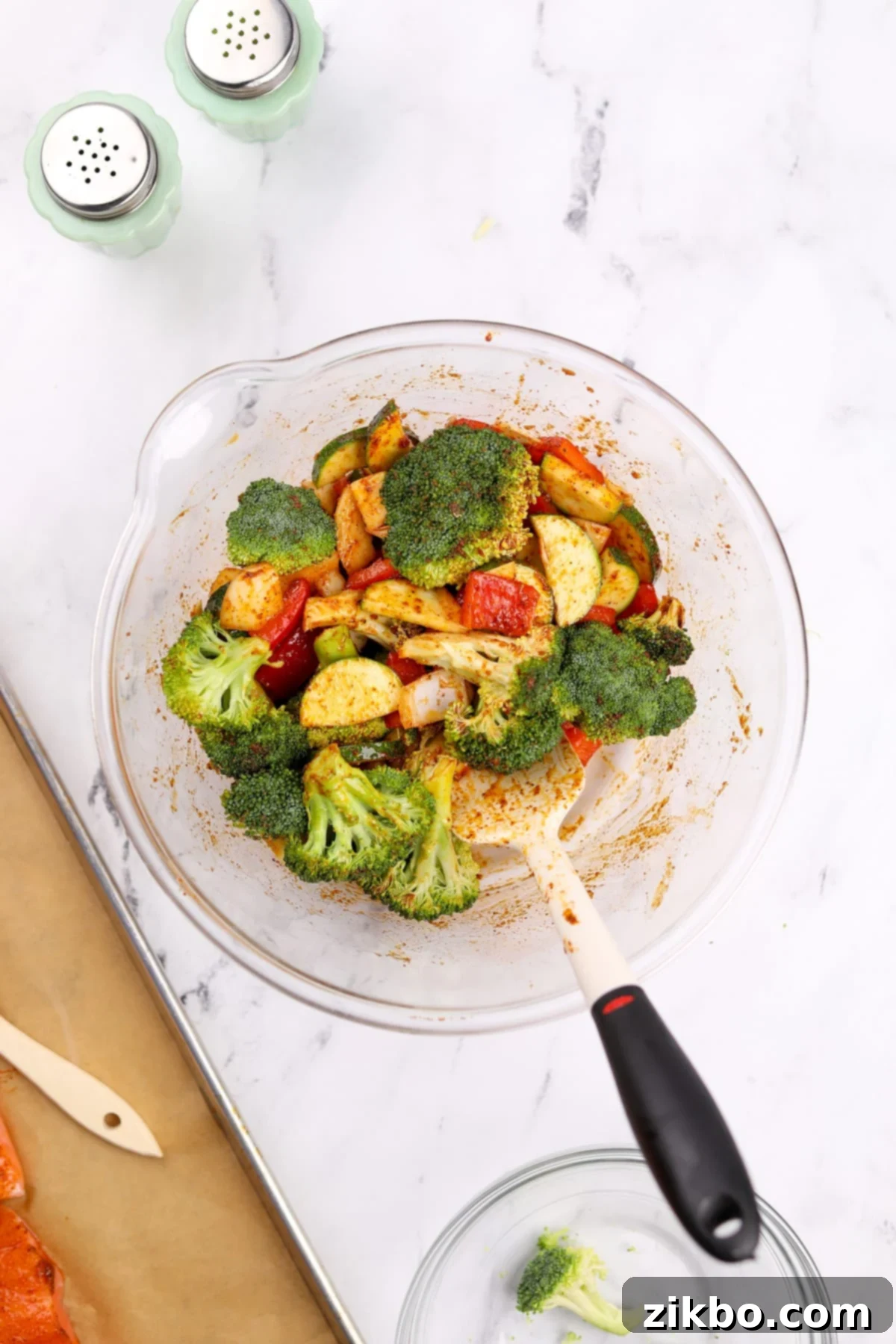 Effortless Sheet Pan Salmon Feast 7 A hand gently tossing the mixed vegetables in a large bowl, ensuring they are evenly coated with the seasoned oil.