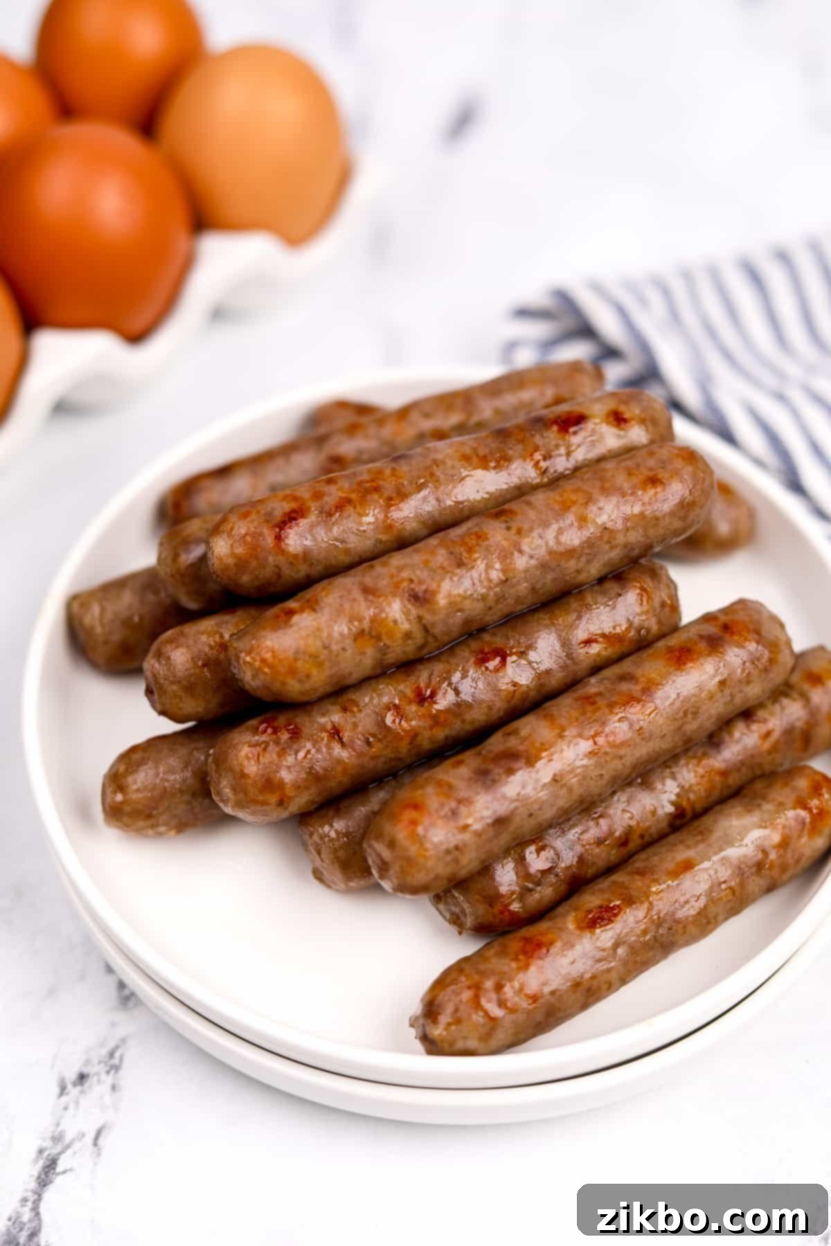 A simple white plate stacked with layers of golden-brown, cooked breakfast sausages, creating an appetizing and satisfying meal.