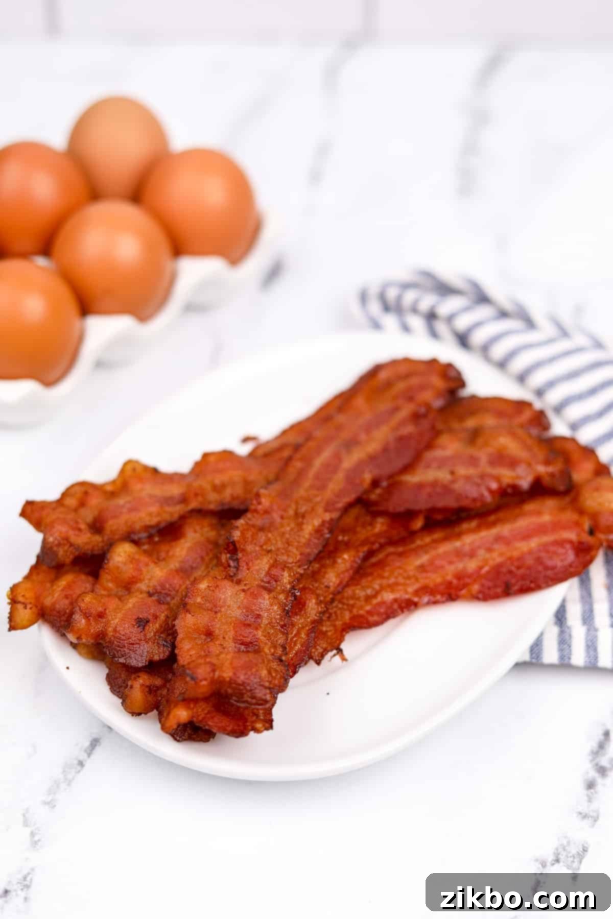 Perfectly Crispy Baked Bacon 6 A white plate piled high with crispy bacon pieces.