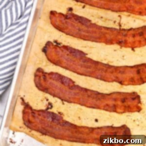 Perfectly Crispy Baked Bacon 9 Slices of crispy bacon on a parchment lined baking sheet.