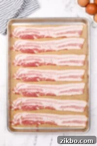 Eight slices of bacon on a parchment lined baking sheet.