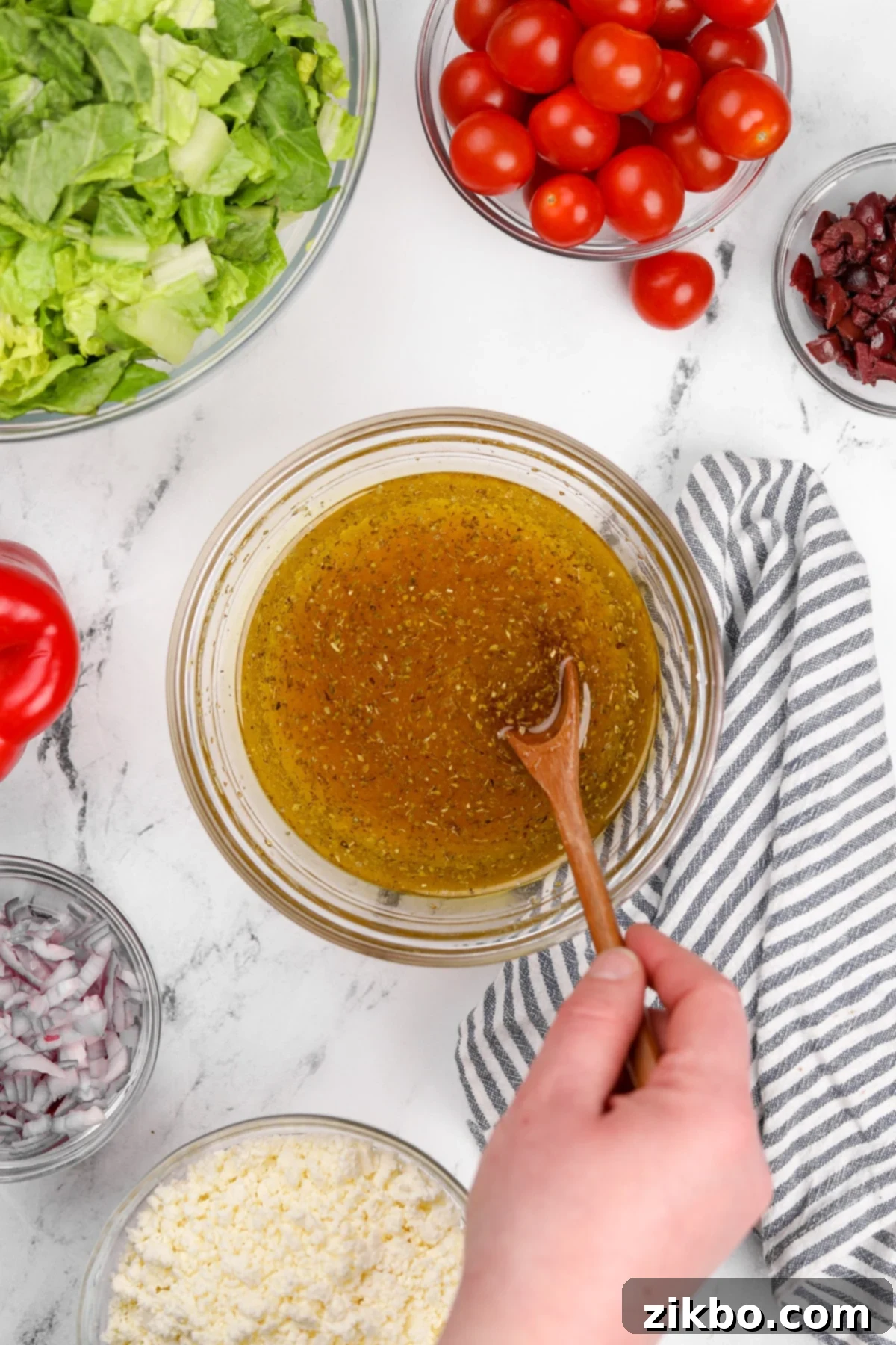 A small bowl with Greek vinaigrette being vigorously stirred with a whisk to combine all the ingredients into a smooth dressing.