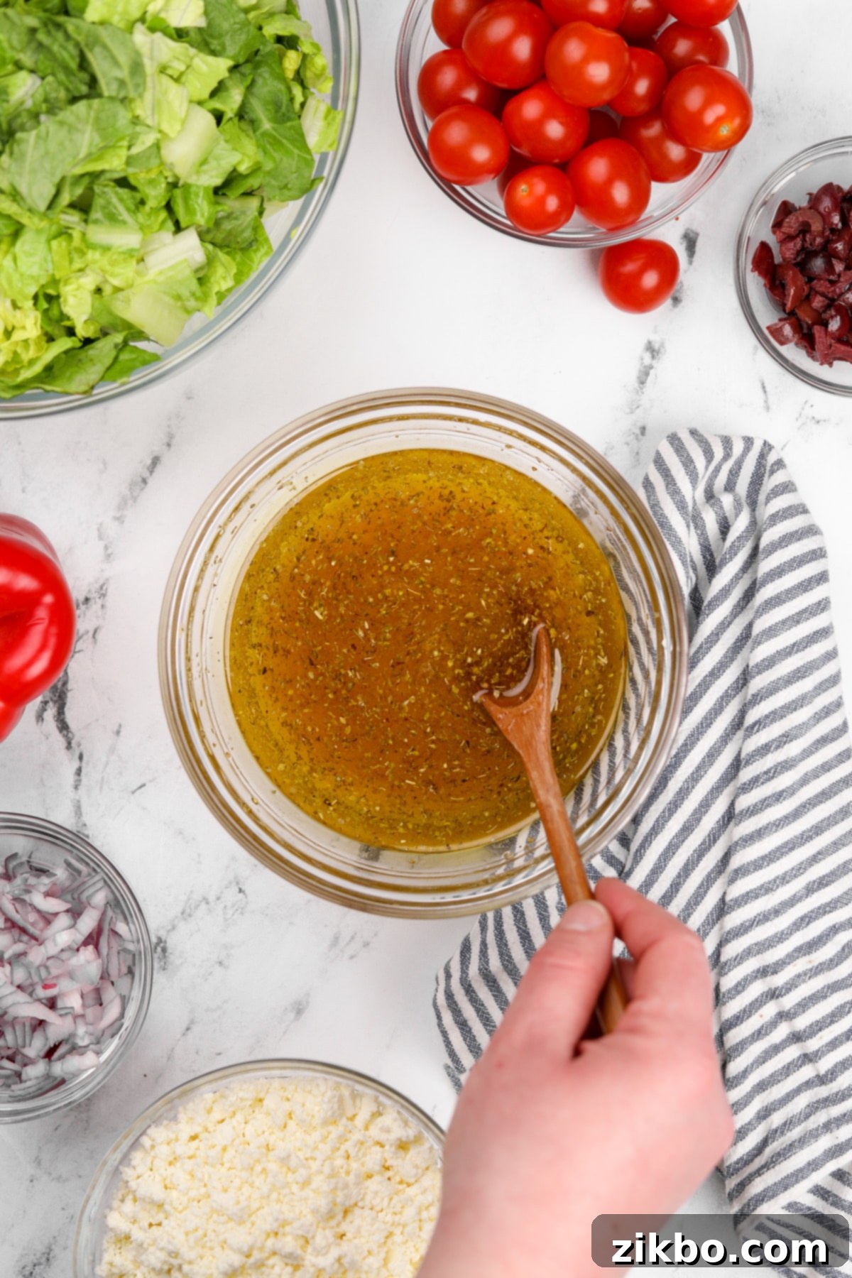 The Perfect Greek Chopped Salad 5 A hand stirring together the ingredients for a homemade salad dressing in a glass bowl.