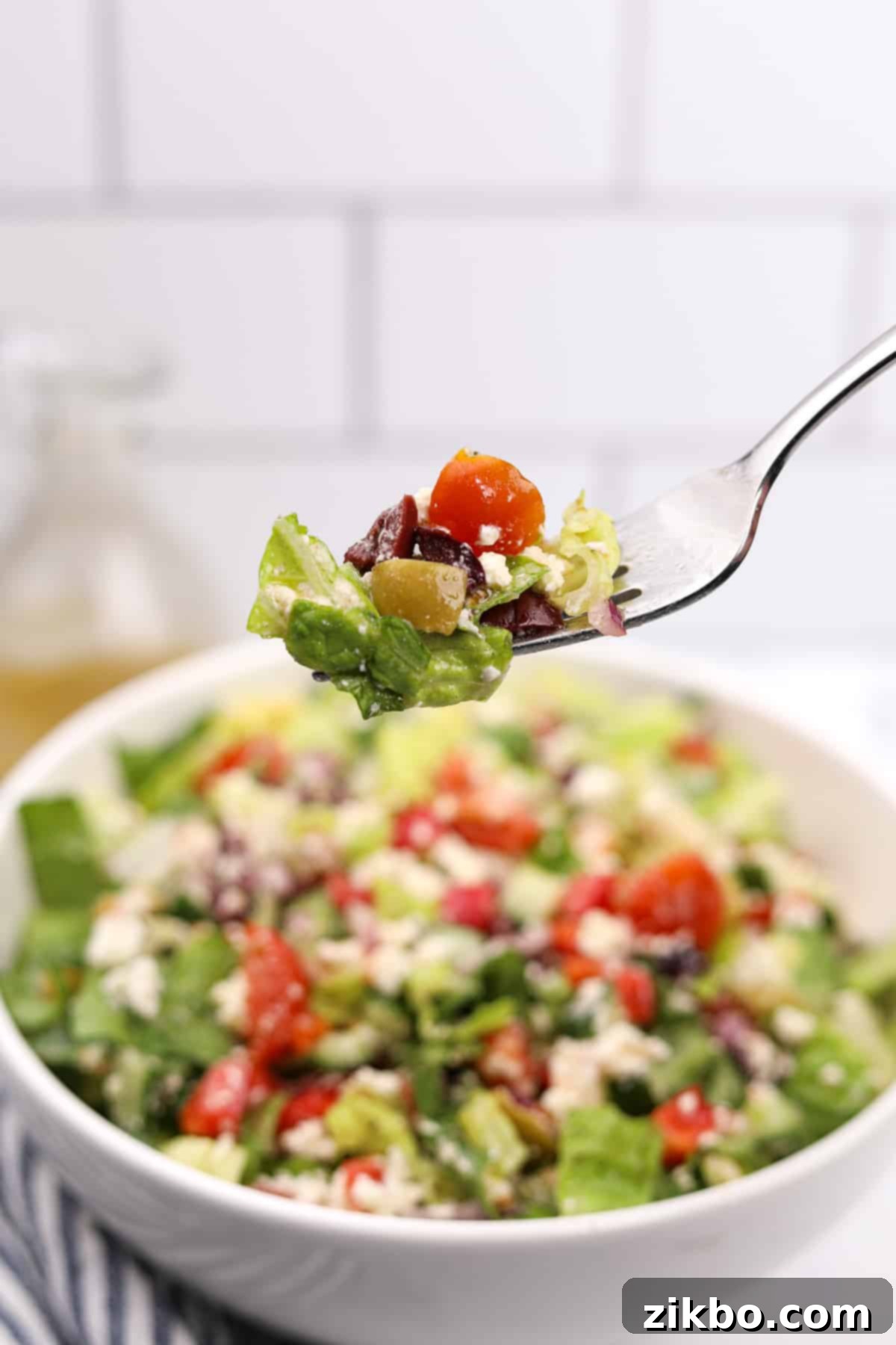 The Perfect Greek Chopped Salad 8 A fork lifting a portion of colorful Greek chopped salad, featuring feta, tomato, cucumber, and olives, emphasizing its deliciousness.