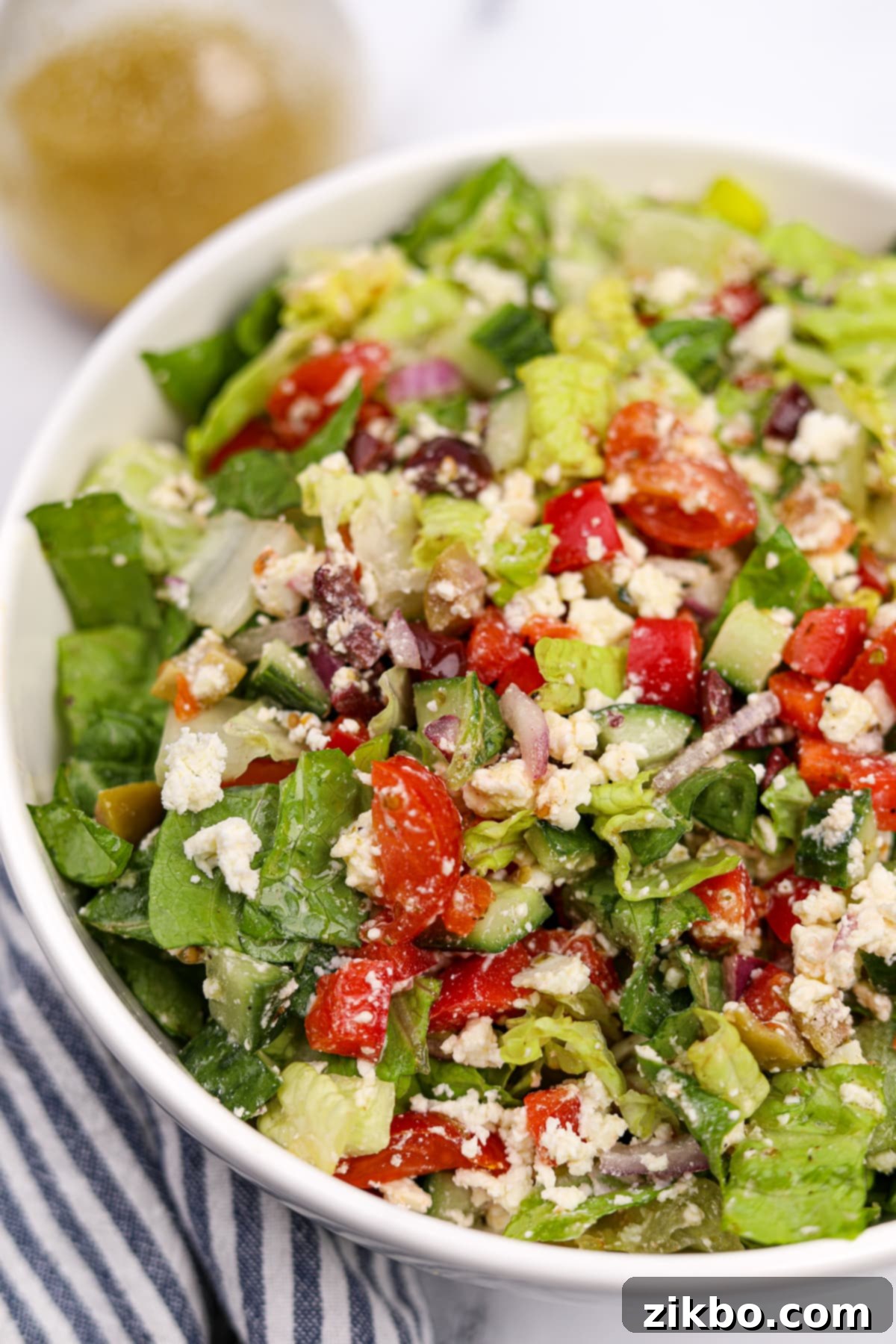 The Perfect Greek Chopped Salad 9 A close-up shot of a bowl of Greek chopped salad, focusing on the textures of feta cheese, ripe tomato, crisp cucumber, briny olives, and fresh romaine lettuce.