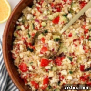 A spoon scooping a portion of Greek quinoa salad from a large wooden bowl.