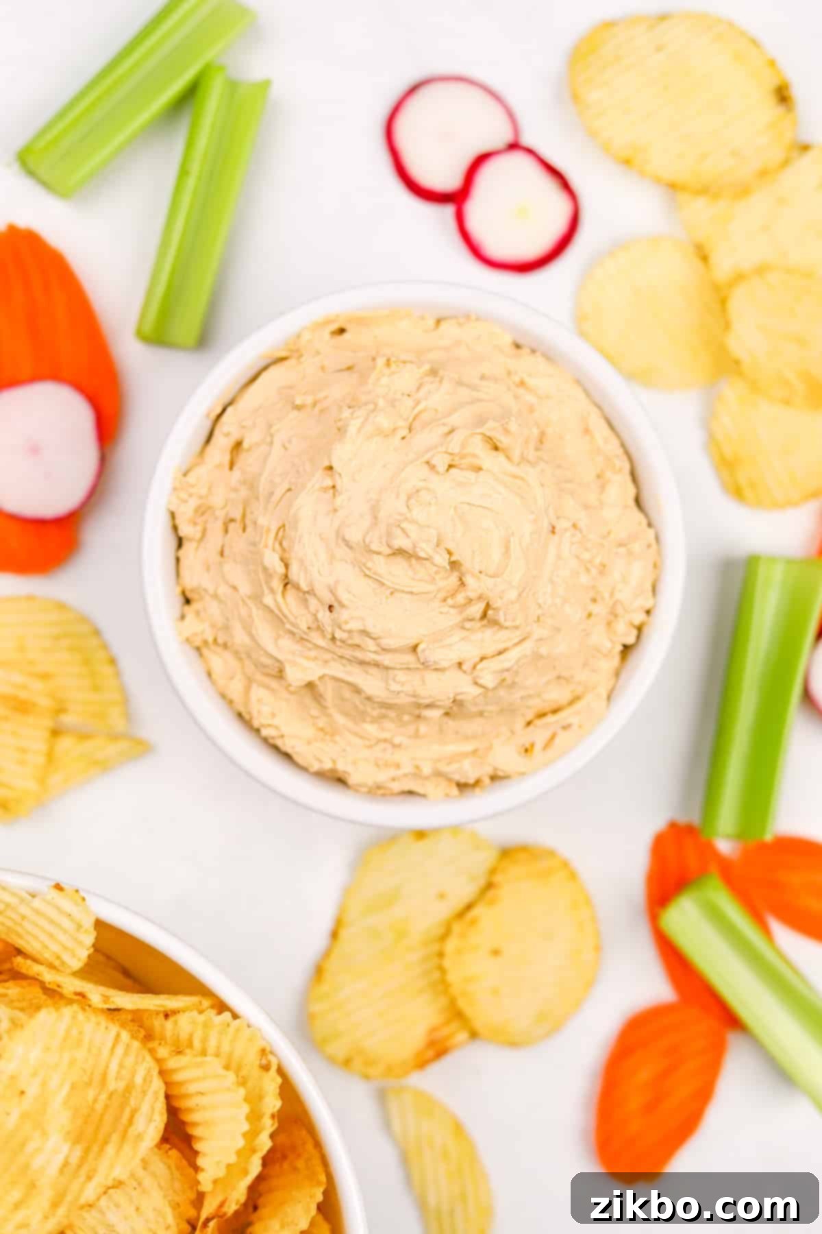 A beautifully presented bowl of creamy French onion dip, surrounded by a colorful array of fresh vegetables and crispy potato chips, ready for dipping.