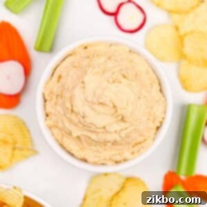 A bowl of creamy California Dip (French Onion Dip), garnished with fresh herbs and surrounded by a variety of vegetables and potato chips, ready to be enjoyed.