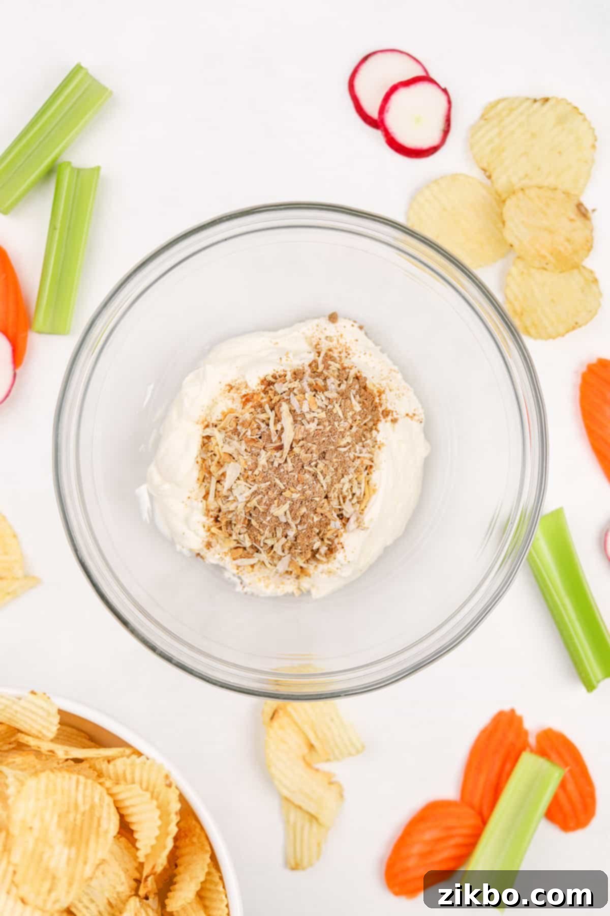 A medium-sized mixing bowl containing a dry packet of onion soup mix on top of creamy sour cream, ready to be combined.