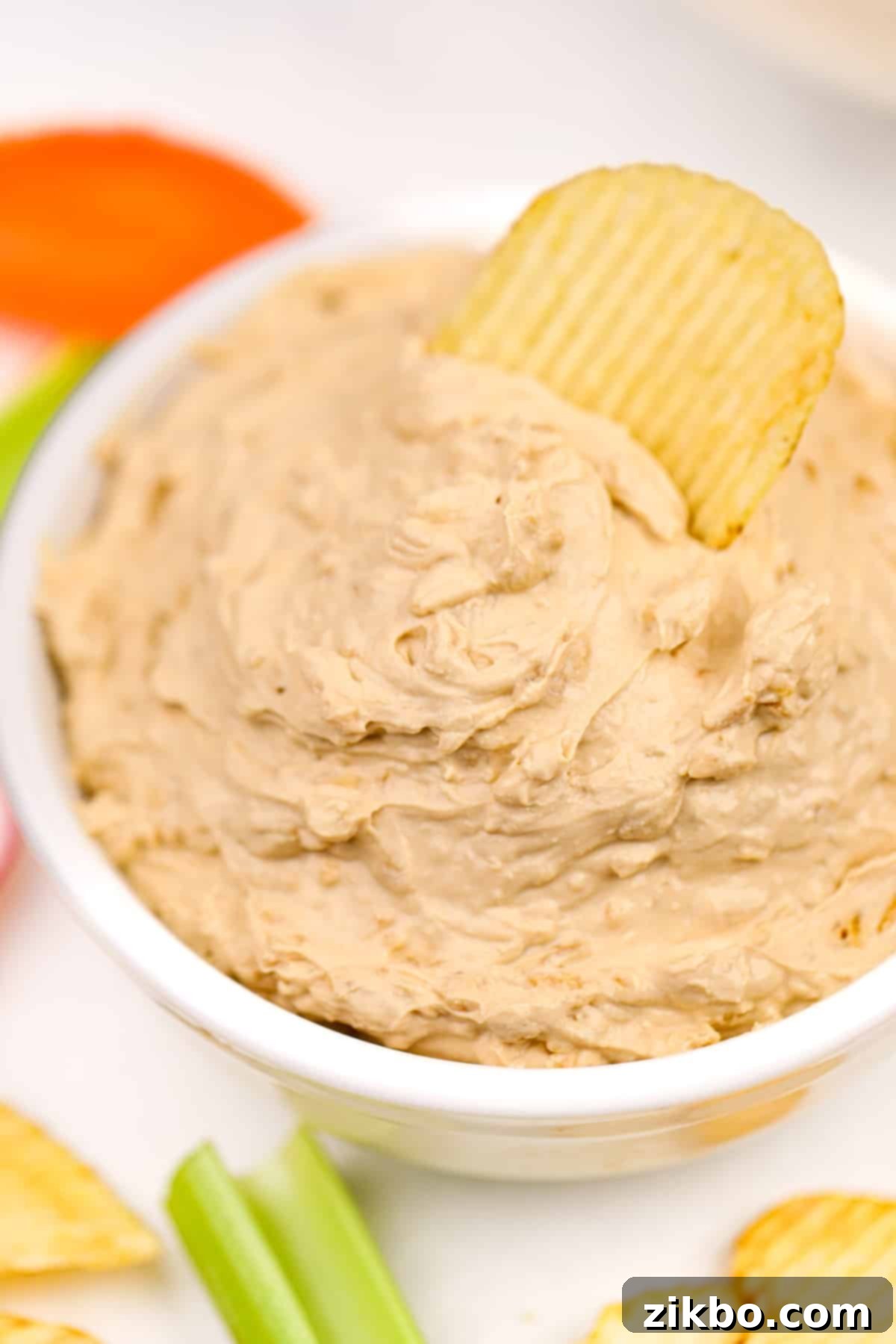 A close-up shot of a crispy potato chip being dipped into a luscious bowl of homemade French onion dip, showcasing its creamy texture.