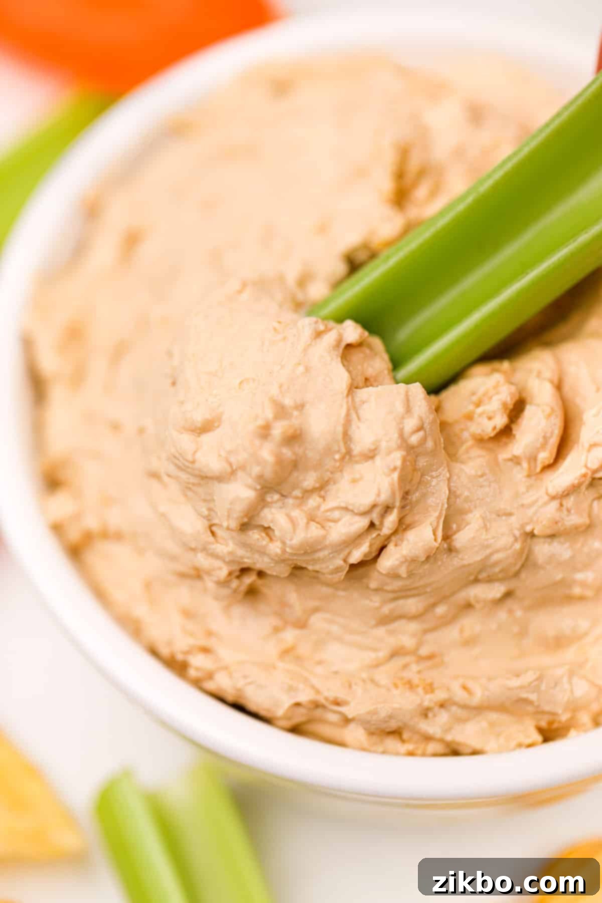 A hand dipping a crisp celery stick into a bowl of creamy, homemade French onion dip, highlighting its perfect dipping consistency.