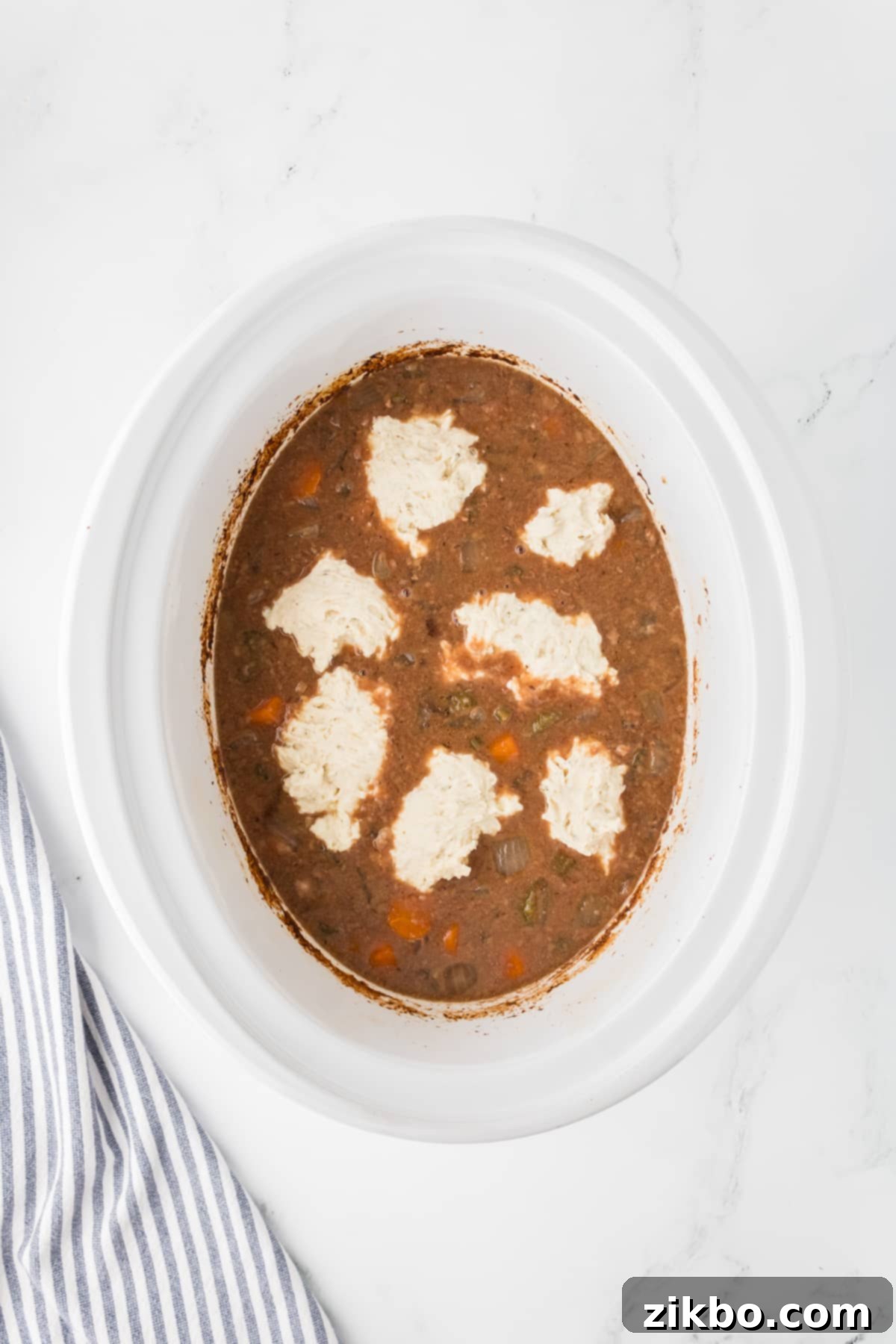 Hearty Slow Cooker Beef Stew with Tender Dumplings 12 A slow cooker insert with dumplings dropped onto the surface of beef stew.