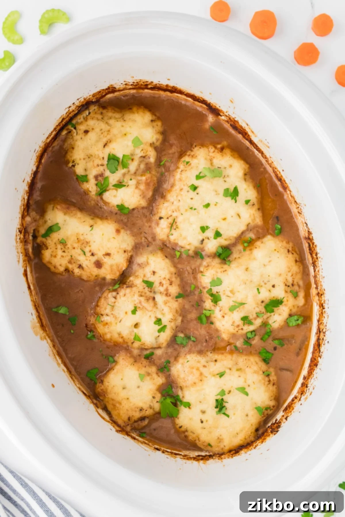 Hearty Slow Cooker Beef Stew with Tender Dumplings 13 A white slow cooker insert filled with beef stew topped with homemade dumplings.