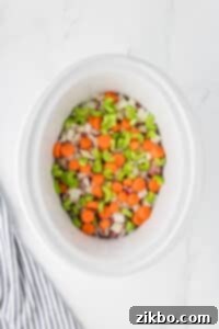 A slow cooker with beef cubes, celery, carrots, and onions layered inside.