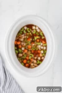 A slow cooker with vegetables and beef broth.