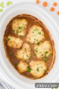A white slow cooker insert filled with beef stew topped with homemade dumplings.