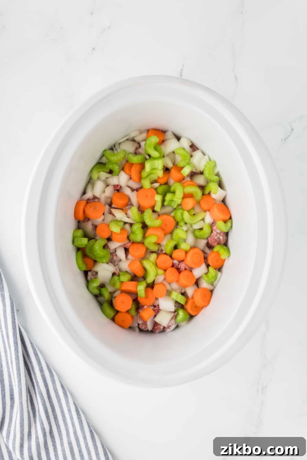 Hearty Slow Cooker Beef Stew with Tender Dumplings 5 A slow cooker with beef cubes, celery, carrots, and onions layered inside.