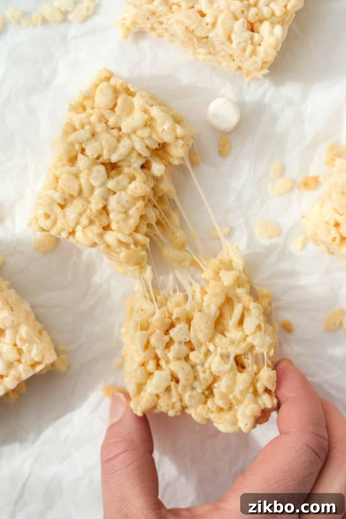 Crispy Sweet Squares 11 A close-up of a Rice Krispie treat being gently pulled apart, revealing its incredibly gooey, stretched marshmallow center, emphasizing its perfect chewy texture.
