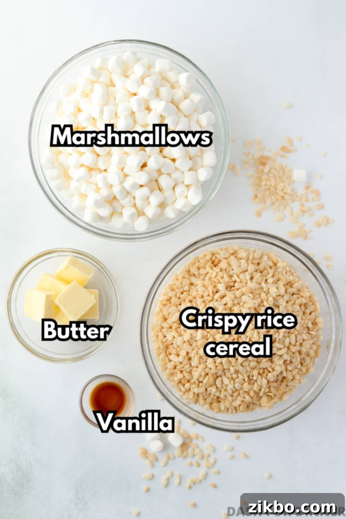 Crispy Sweet Squares 3 A beautifully arranged selection of the four essential ingredients: a bowl of fluffy mini marshmallows, a bowl of crispy rice cereal, cubes of rich butter, and a small dish of aromatic vanilla extract.