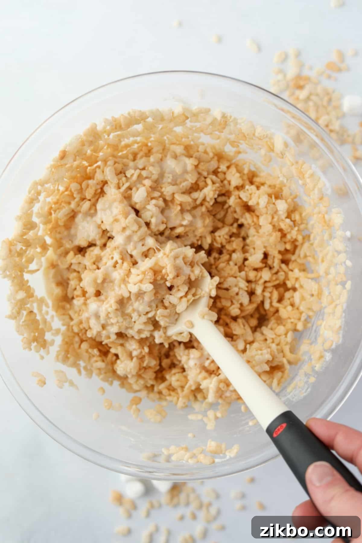 Crispy Sweet Squares 7 Crispy rice cereal being gently folded into the warm, gooey marshmallow mixture with a silicone spatula, ensuring every piece is coated.