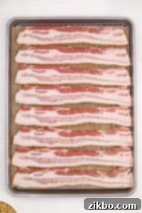 Raw bacon strips in an even layer on a wire rack set inside of a baking pan.