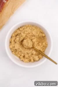A small bowl of brown sugar being mixed with a small gold spoon.