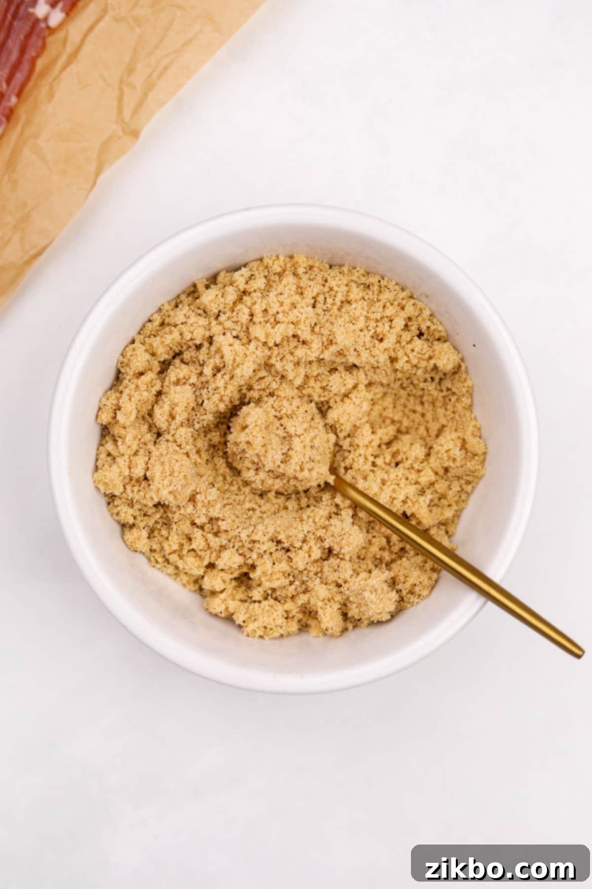 Millionaire's Bacon 5 A small gold spoon is actively mixing brown sugar and black pepper in a small bowl until thoroughly combined.
