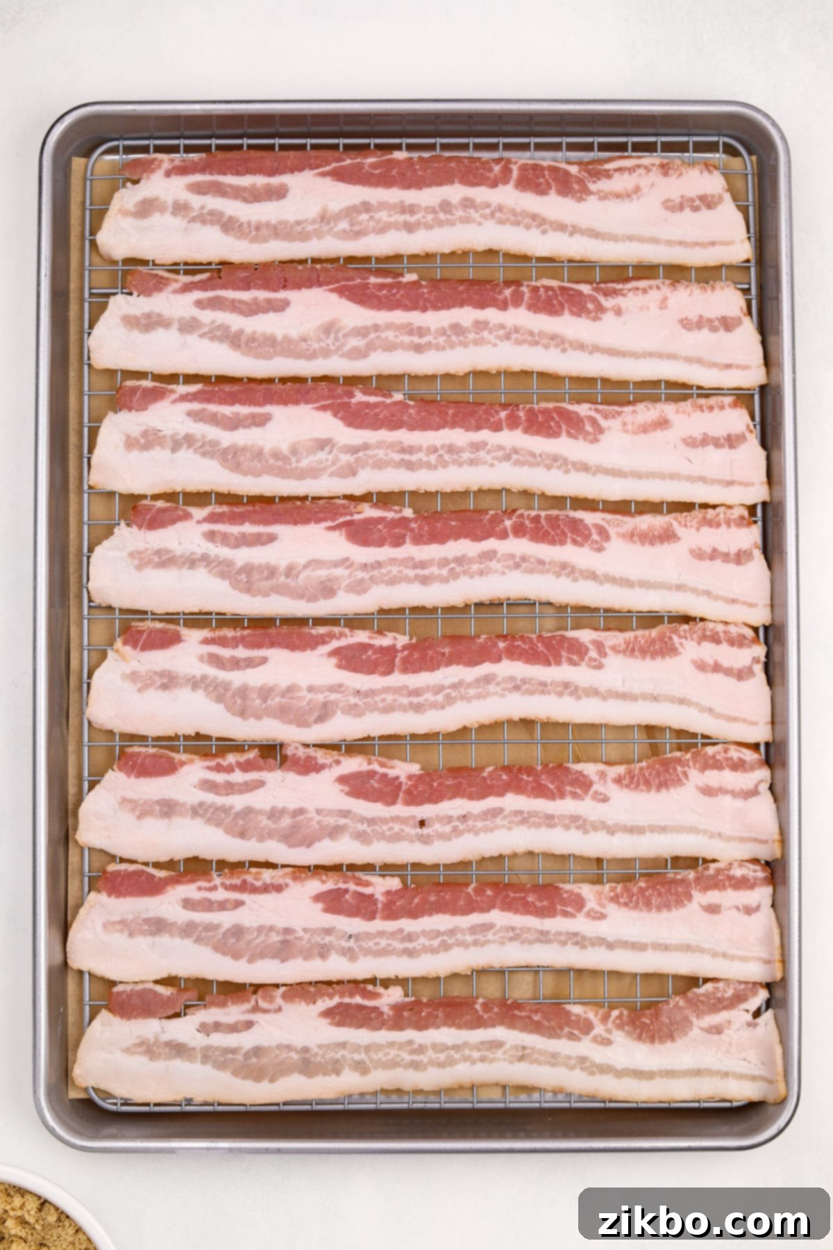 Millionaire's Bacon 6 Raw bacon strips are laid out in a single, even layer on a wire rack, which is placed inside a parchment-lined baking sheet.