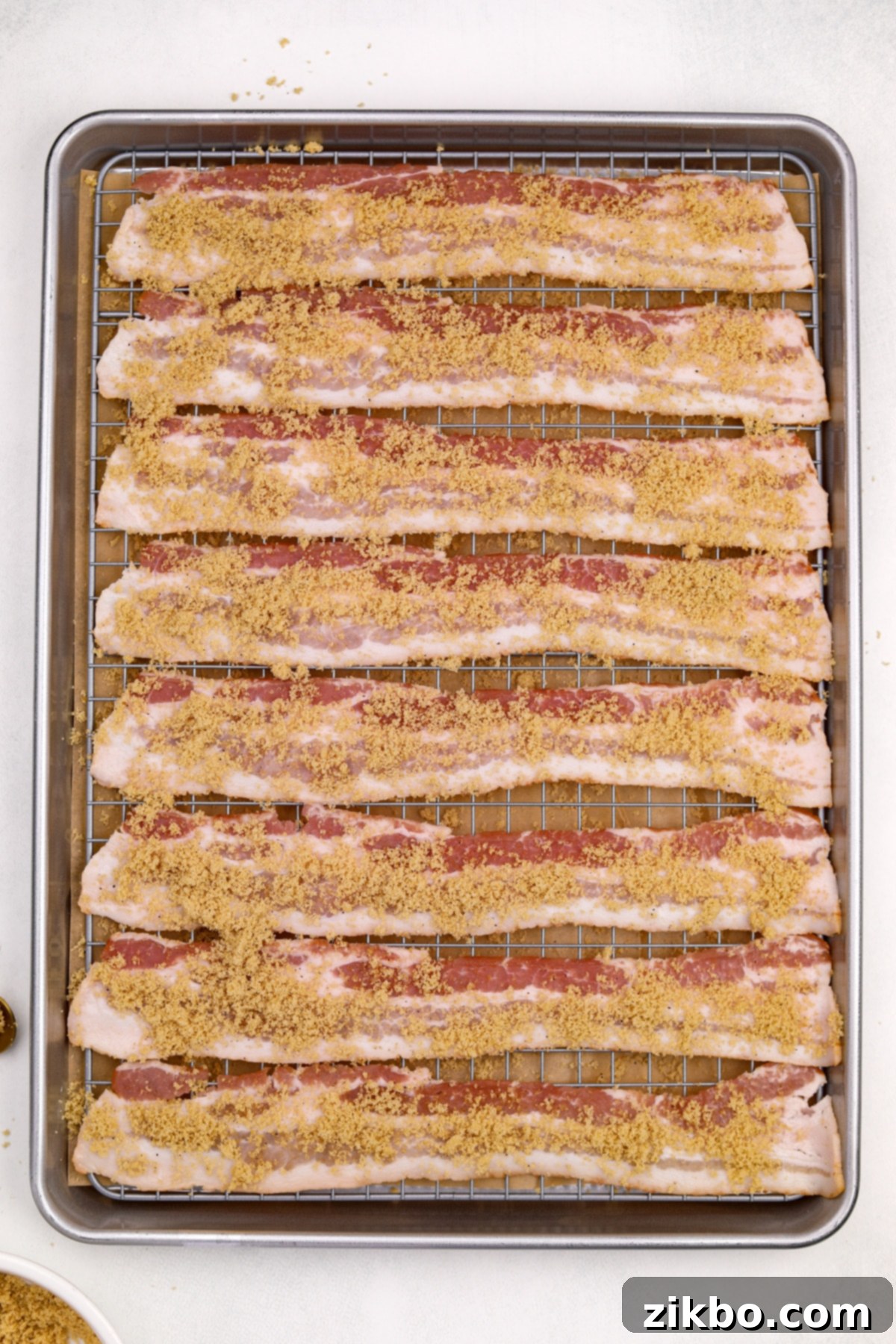 Millionaire's Bacon 7 Raw bacon strips on a wire rack are generously covered with an even layer of brown sugar and black pepper mixture.