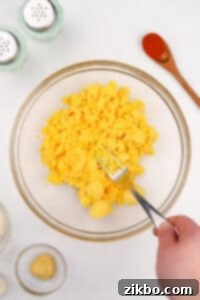 Mashing cooked egg yolks in a bowl with a fork.