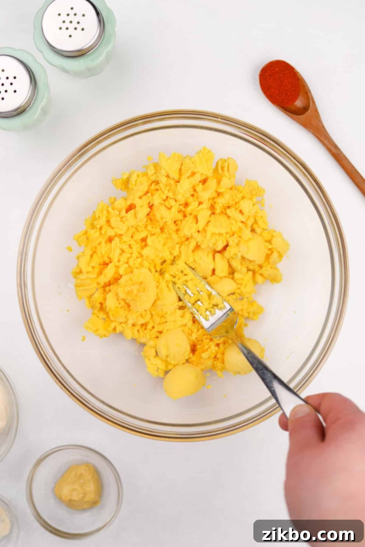 Mashing cooked egg yolks in a bowl with a fork.