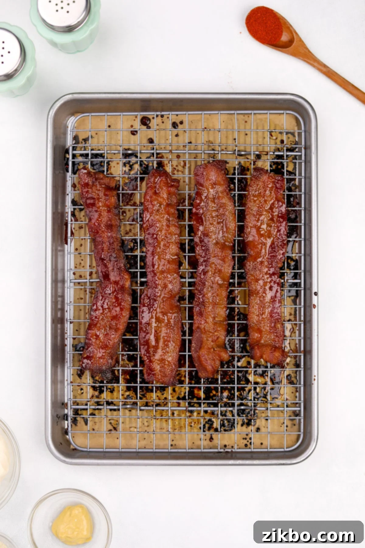 Four perfectly cooked and caramelized slices of candied bacon resting on a baking sheet, glistening with sugar.