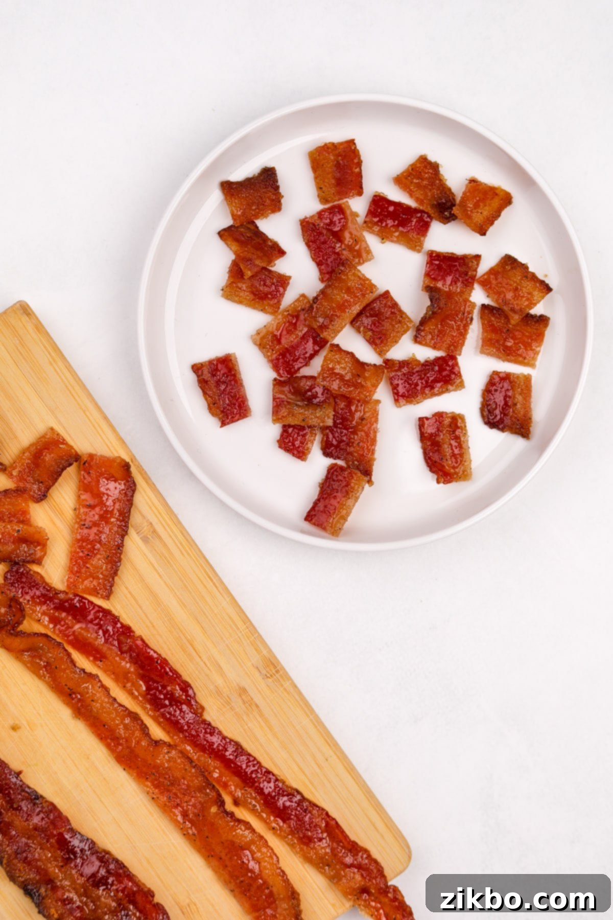 Crispy candied bacon being expertly chopped into small 1" cubes on a cutting board, ready for garnish.