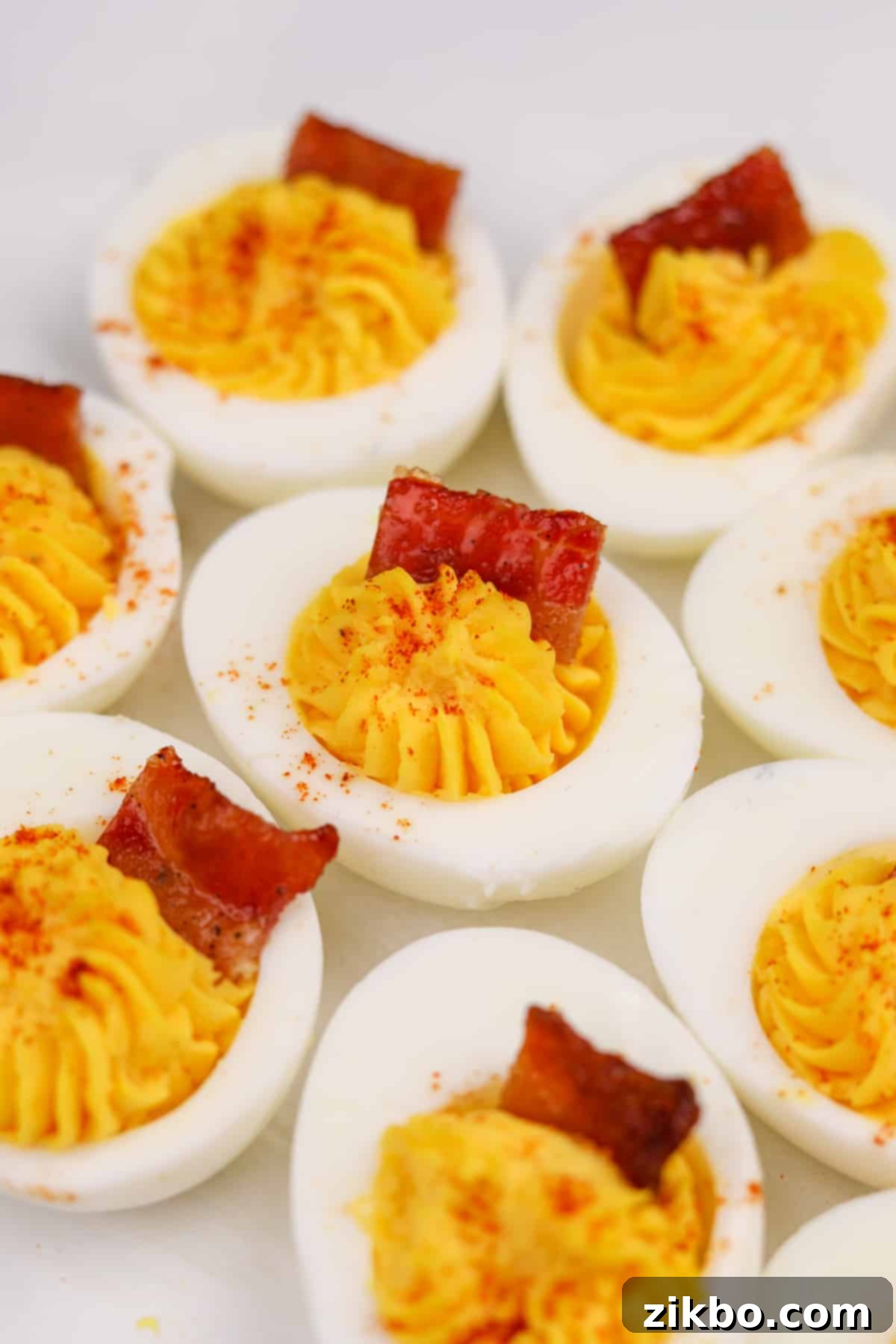 A close-up of a deviled egg half, beautifully filled and garnished with a piece of candied bacon, showcasing its sweet and savory appeal.