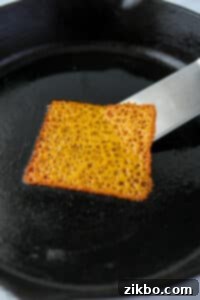Using a spatula to loosen a melted cheese slice from a spatula.